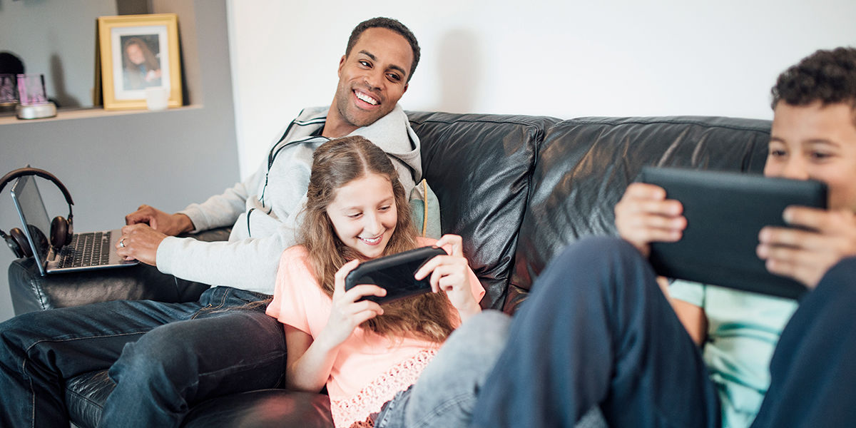 Father happily watching kids playing handled game